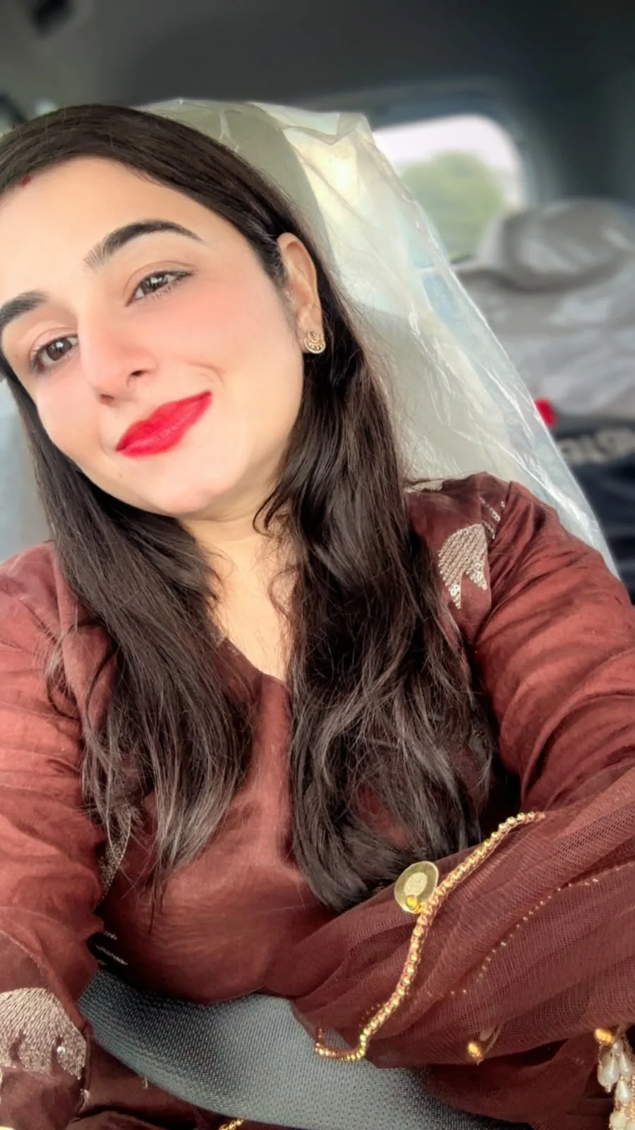 Puru wearing a brown embroidered outfit and smiling while seated in a car